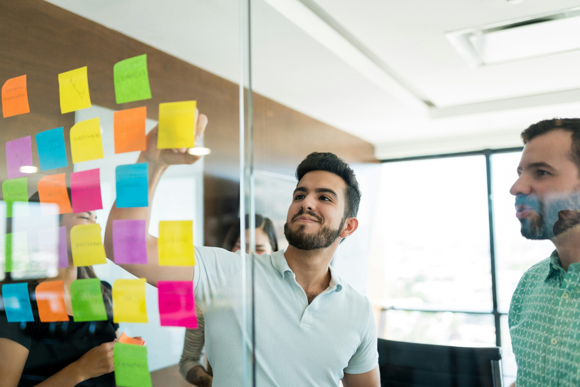 A team collaborating at a glass wall covered in colorful sticky notes planning a campaign